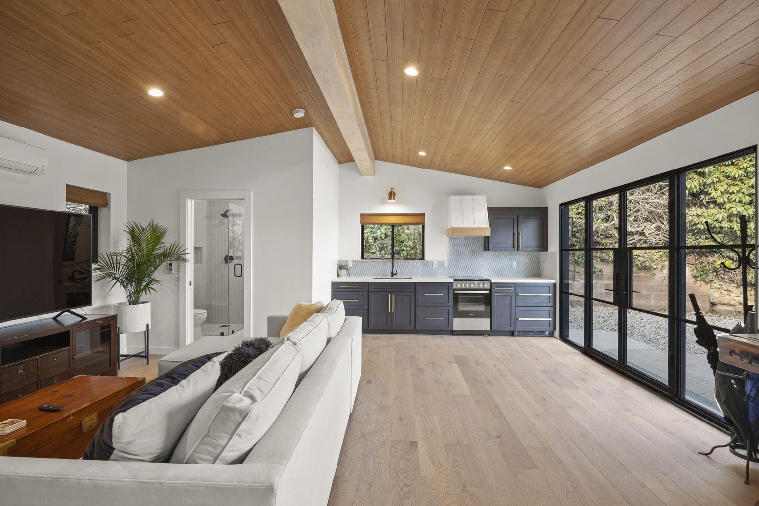 Open-concept living and kitchen space with wood ceiling, white sectional and navy cabinetry