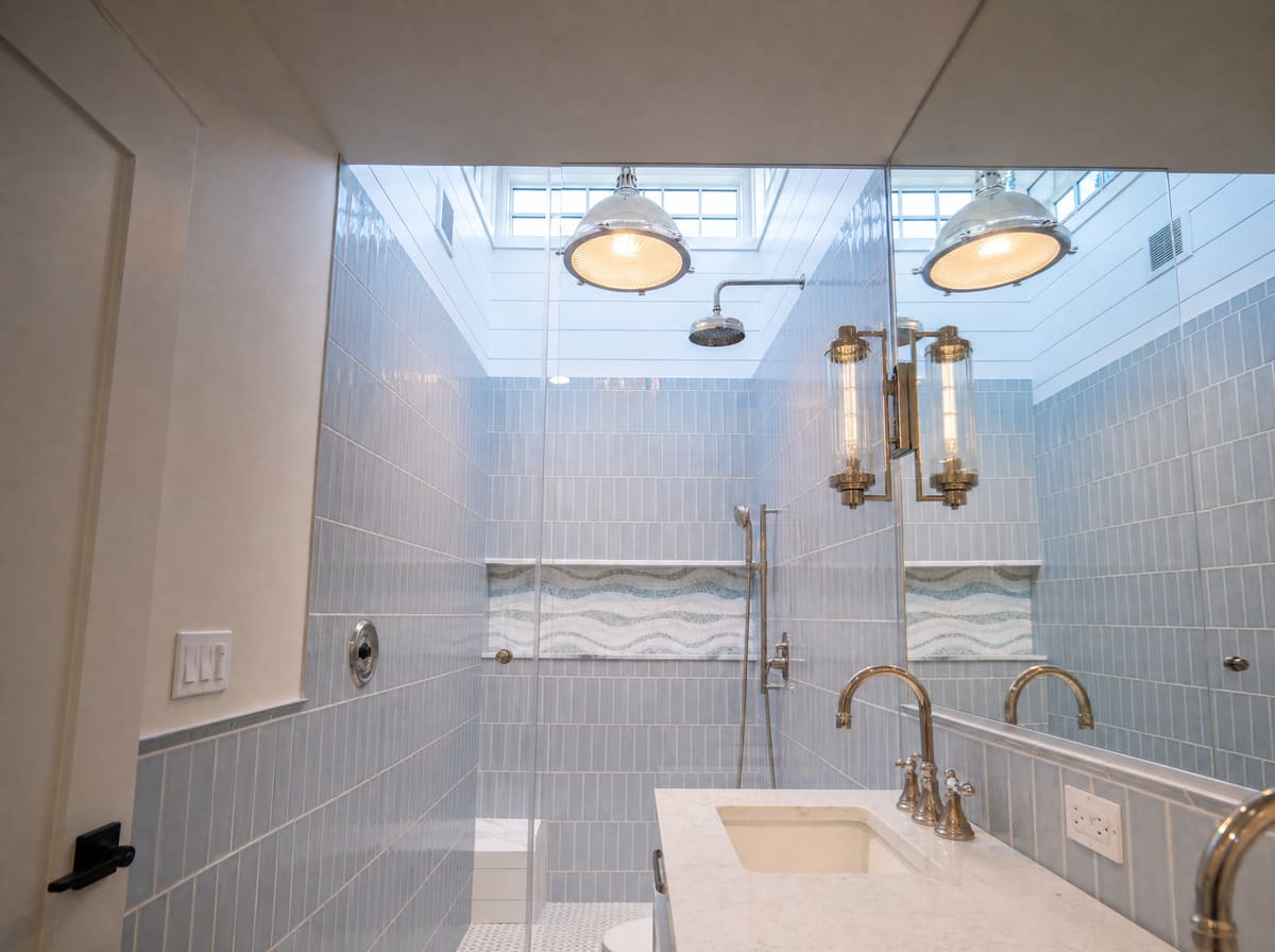 Skylit walk-in shower with blue tile and brass fixtures in a primary bath