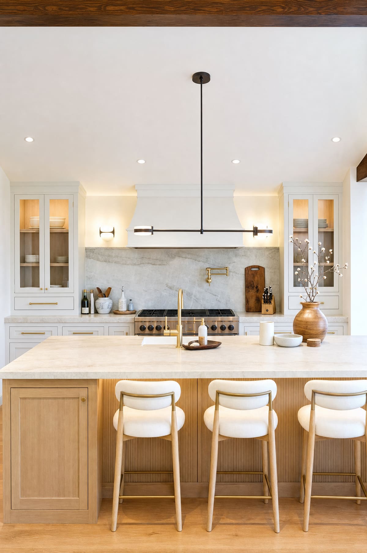 Kitchen island with bar seating beneath a linear pendant, marble backsplash and gas range