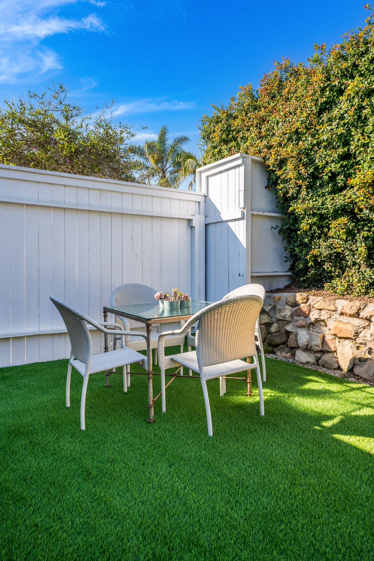 Backyard patio with a dining set on turf, bordered by a stone wall