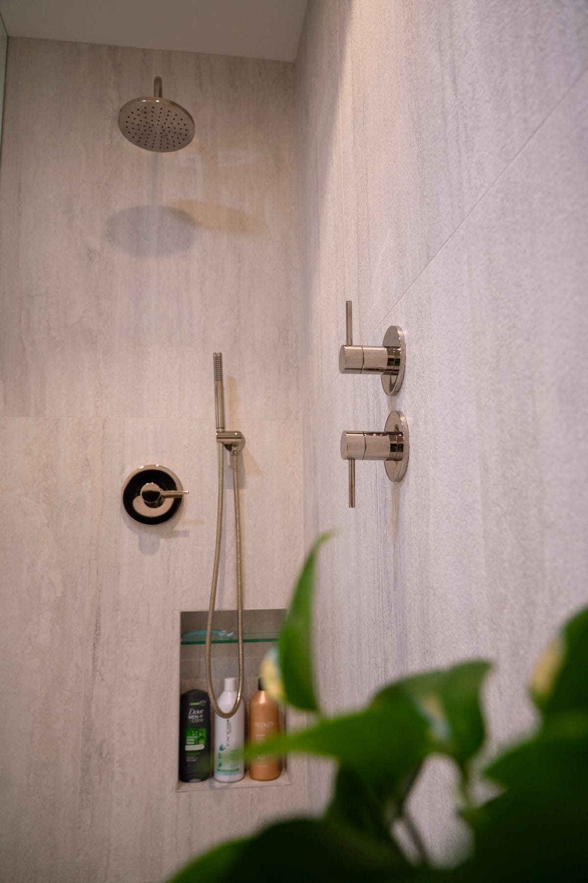 Rain shower head and controls beside a potted plant on stone tile